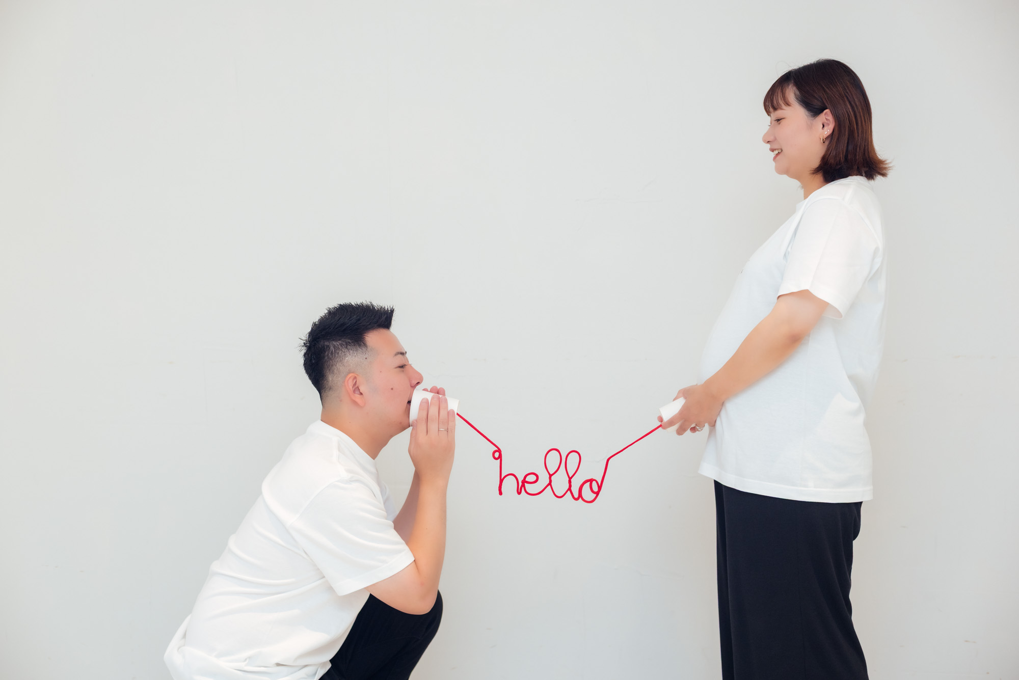 赤い糸の電話で、パパがママのおなかに「hello」と話しかけている写真