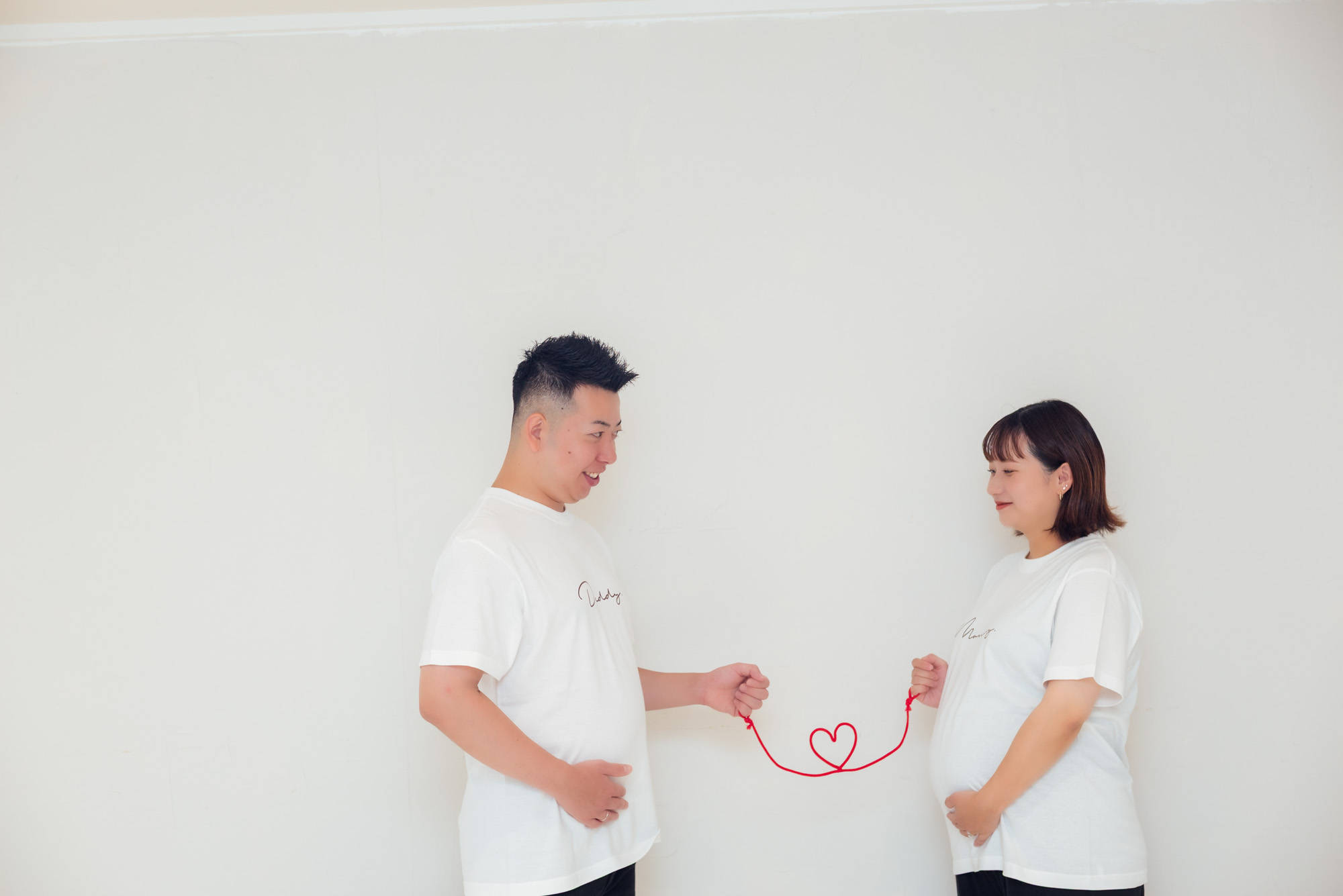 パパとママが赤い糸でつながり、糸がハートの形になっている写真